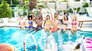 friends sitting at hotel swimming pool wearing swim clothes - Summer life style concept with trendy people having fun on sunny day at luxury poolside