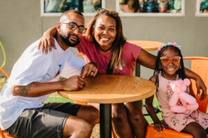 La Porte Family Brittany Golden - Texas Hotel and Lodging Family of three at an outdoor table, smiling for the camera.