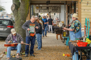 La Porte Main Street Thomas Park - Texas Hotel and Lodging Outdoor street market with musicians playing guitars as shoppers browse colorful stalls under string lights.