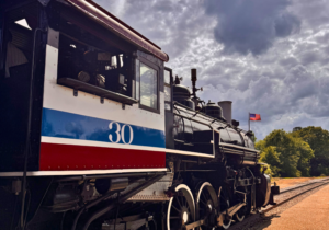 Visit Palestine_4 - Texas Hotel and Lodging Vintage steam locomotive numbered 30 on a track under a cloudy sky, with an American flag in the distance.