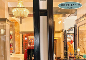 Visit Palestine_8 - Texas Hotel and Lodging Display window of The Redlands Hotel showcasing a large crystal chandelier, warm lighting, and vintage furnishings through glass doors.